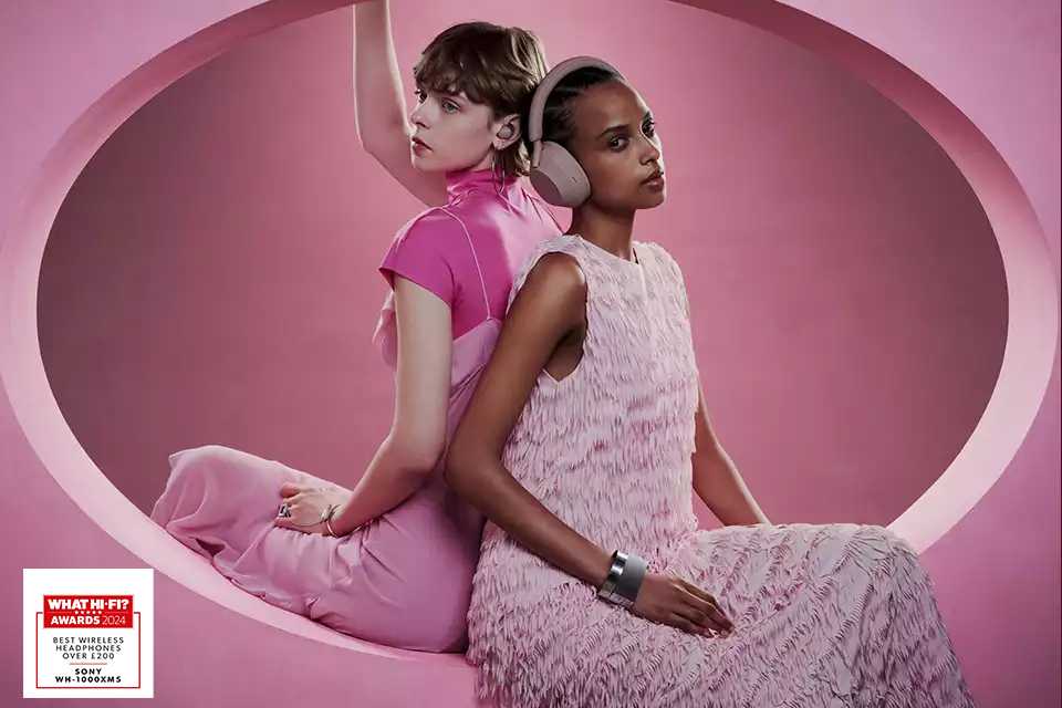 Two women seated back to back, listening to music on a Sony lilac wireless headphones.