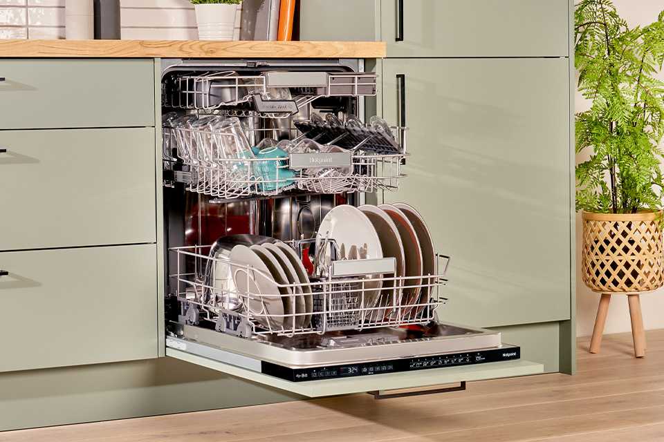 Hotpoint full size dishwasher seamlessly built into modern green kitchen cabinets.