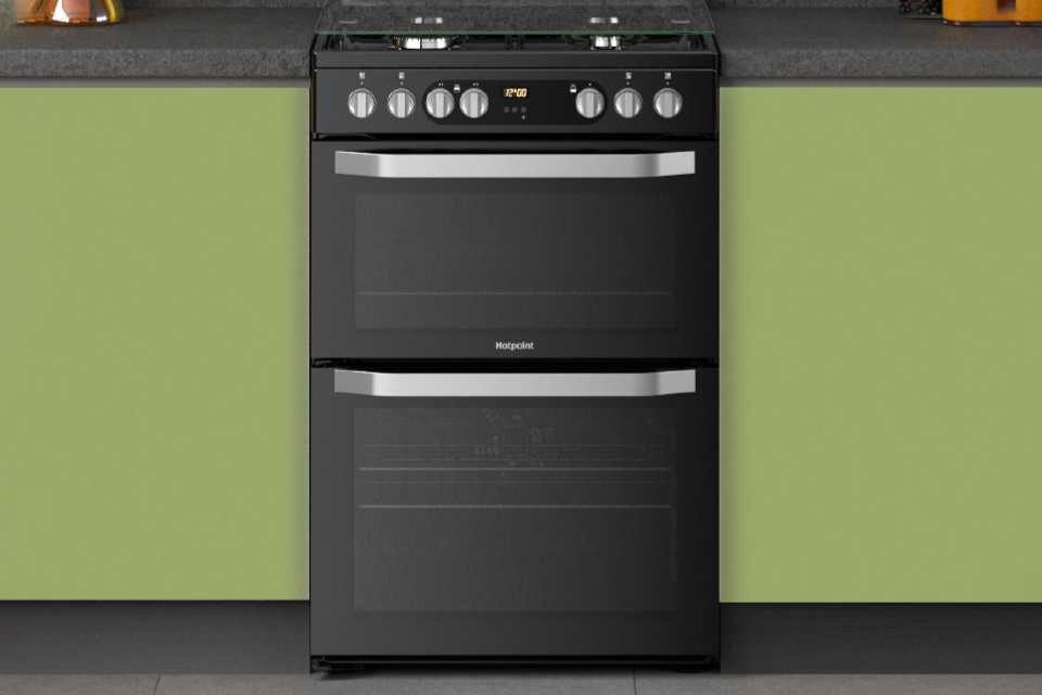 Hotpoint black freestanding cooker with double oven built into modern green kitchen cabinets.
