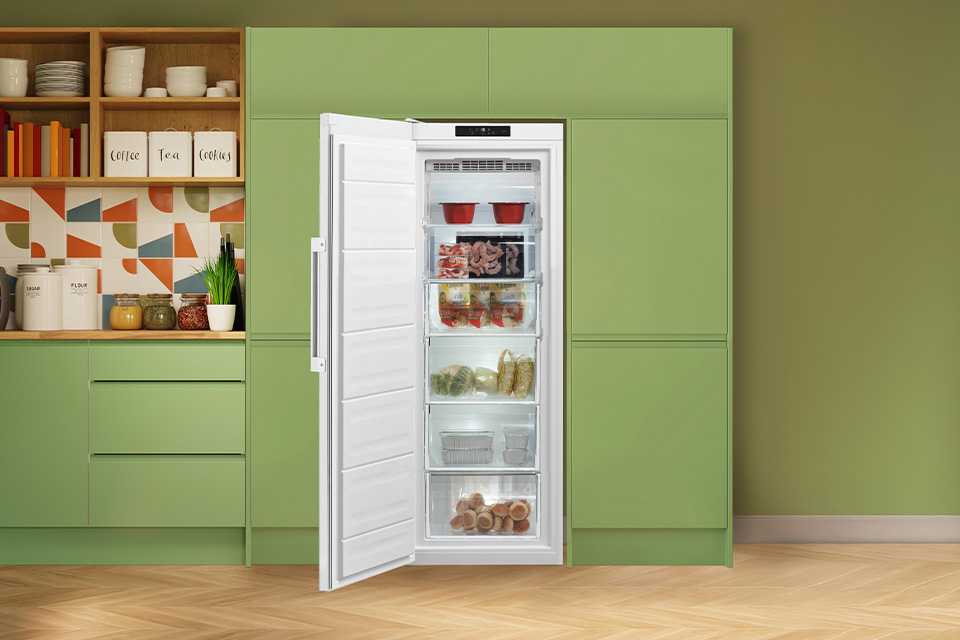 A Hotpoint white freezer seamlessly built into modern green kitchen cabinets.
