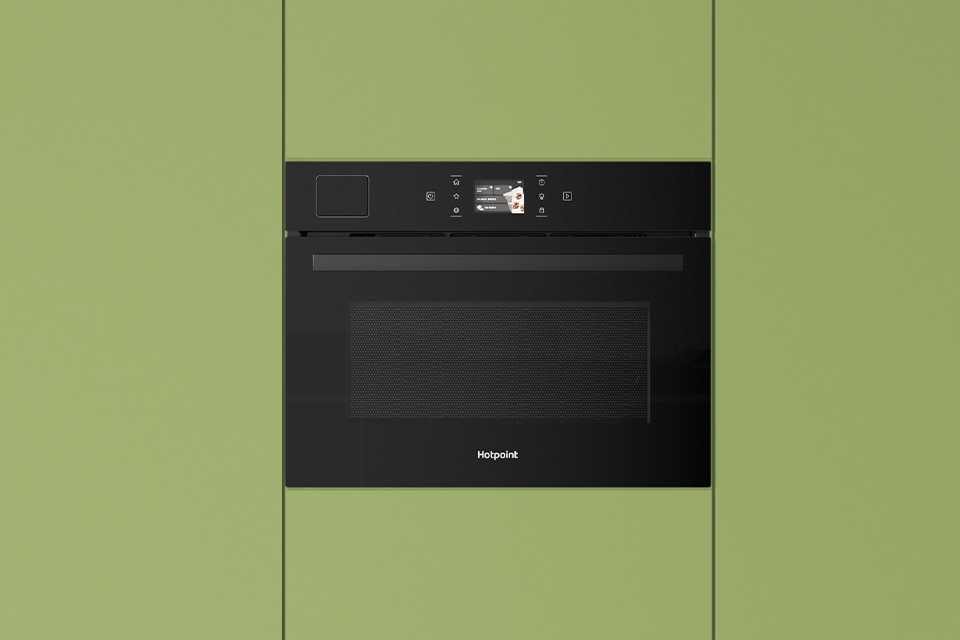 Hotpoint black microwave built into modern green kitchen cabinets.