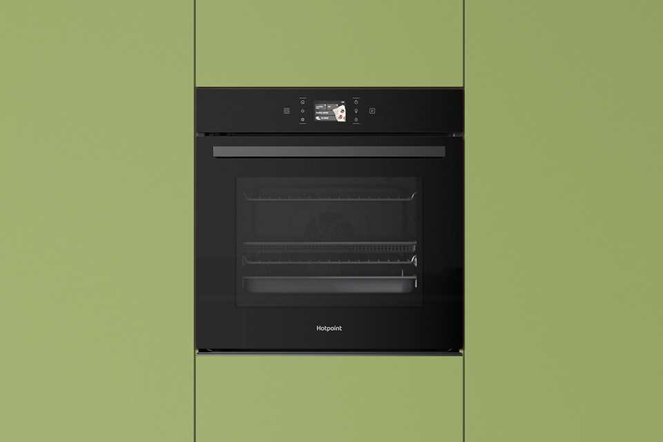 Hotpoint black oven built into modern green kitchen cabinets.