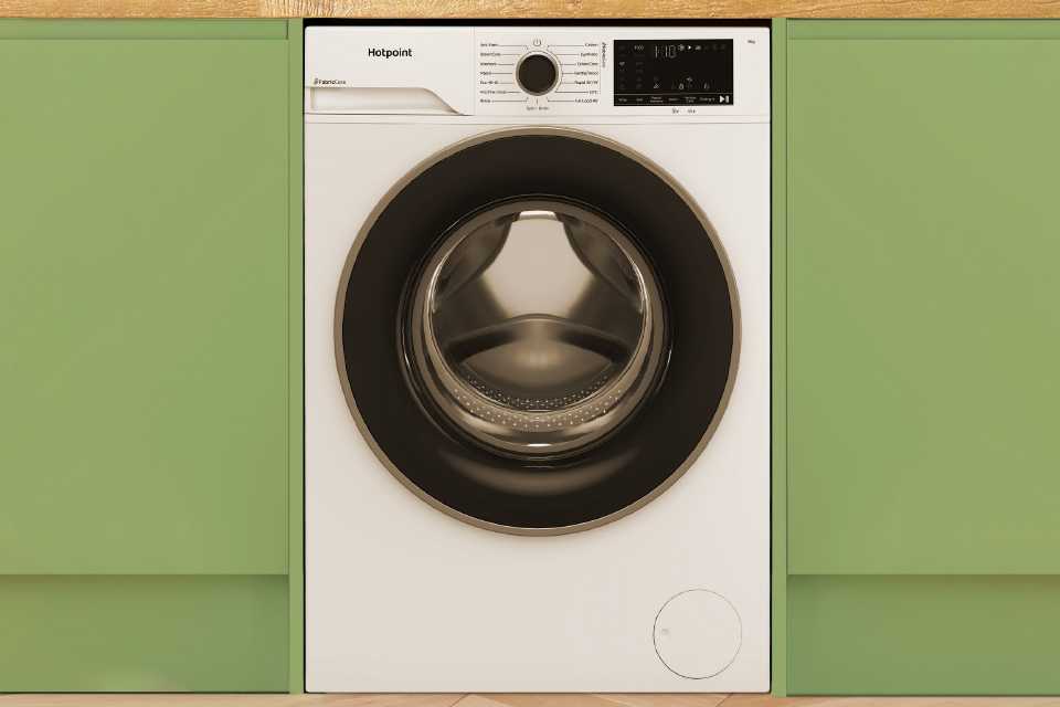 A Hotpoint white washing machine seamlessly built into modern green kitchen cabinets.