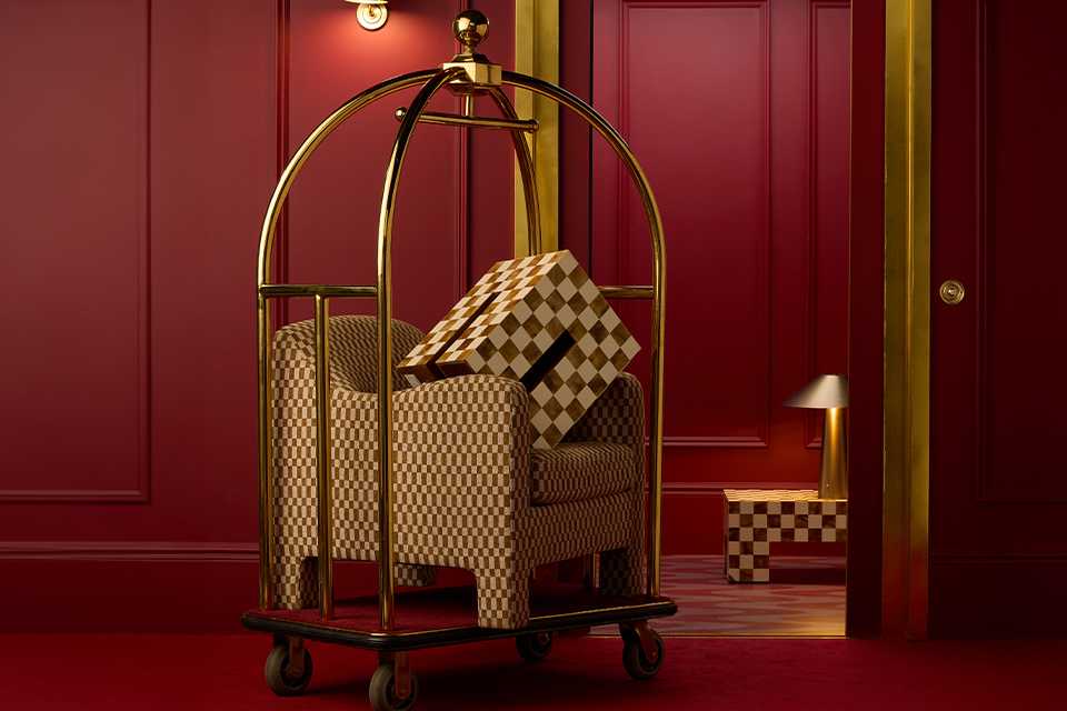 A trolley in a hotel lobby with a chequered box on top of a chequered sofa next to a table lamp on a chequered coffee table.