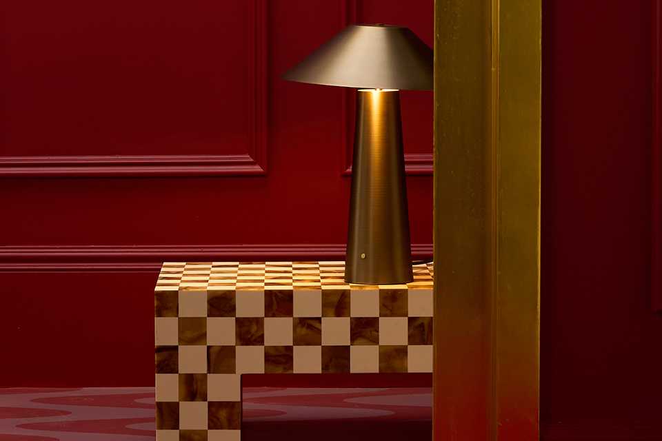 A gold Habitat table lamp on top of a chequered coffee table placed in a hotel lift.