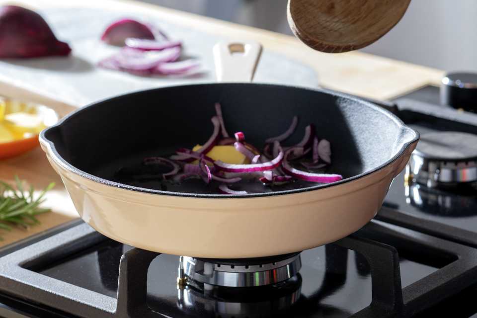A person cooking with the Habitat cast iron frying pan with enamel coating.