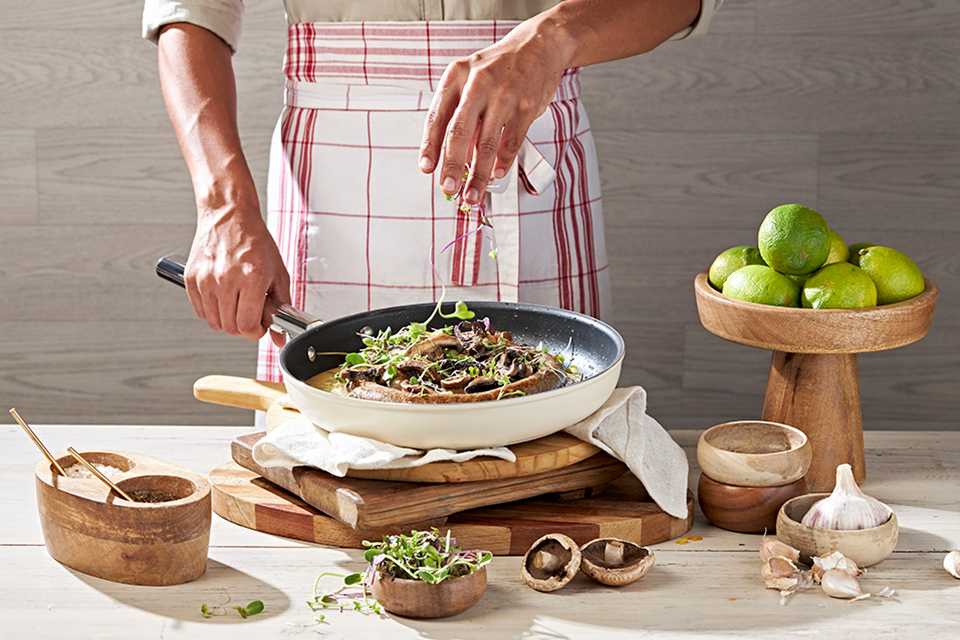 Man sprinkling greens into Smeg cream frying pan.