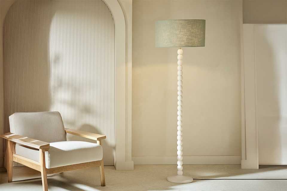 A Habitat Bobbin Mango Wood Floor Lamp Base Only - Ivory near an armchair.