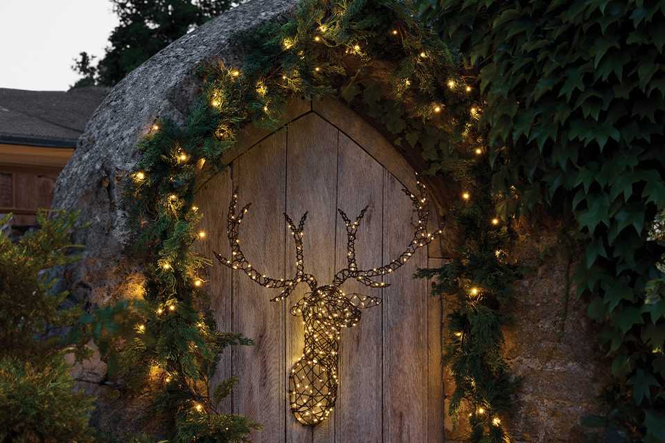Light up stag head hanging on an outside gate surrounded by a garland with lights
