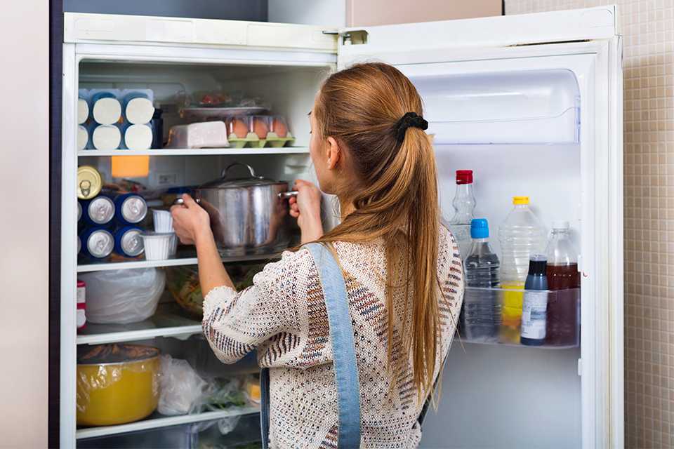 A girl keeping a utensil inside a full fridge.