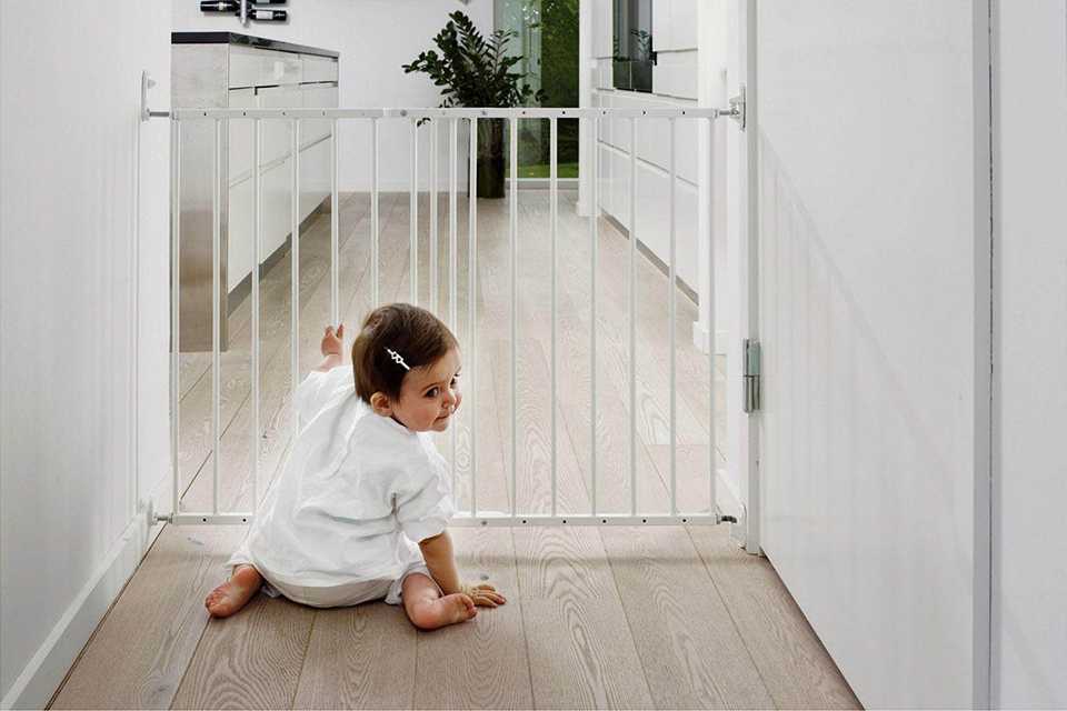 A baby holding a white safety gate.