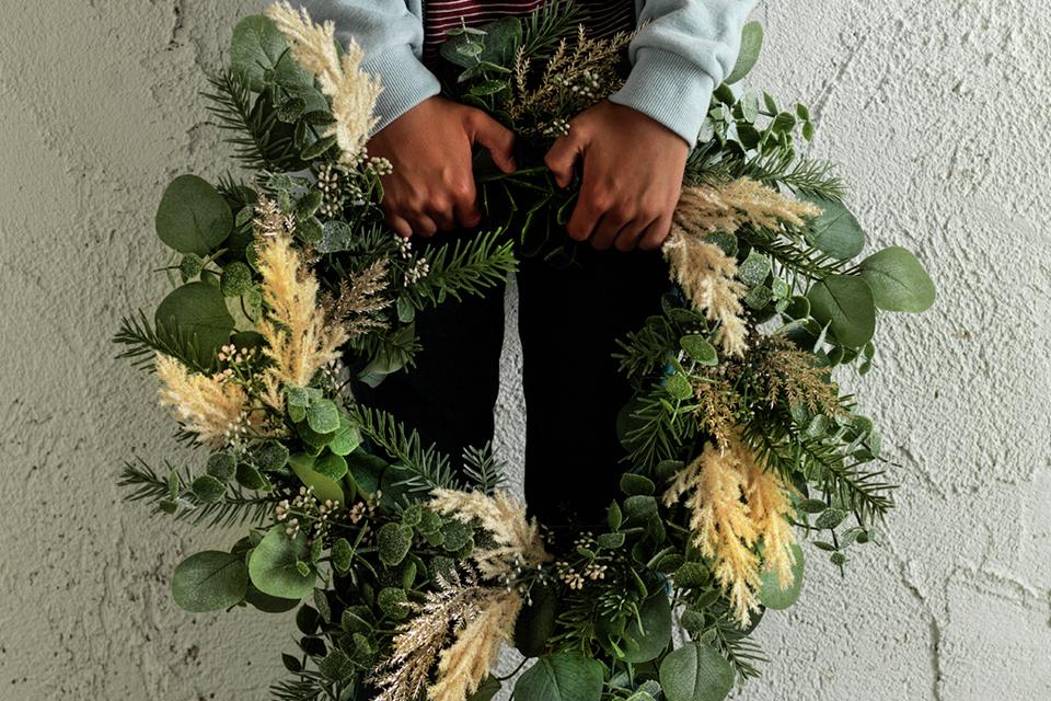 A child holds a foliage-style Christmas wreath.