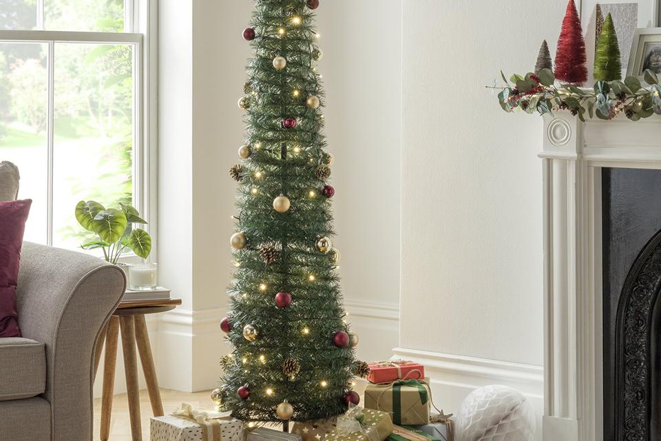 A pop-up lit Christmas tree placed next to a sofa.