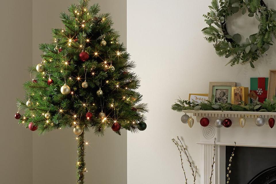 A half parasol Christmas tree placed next to a fireplace.