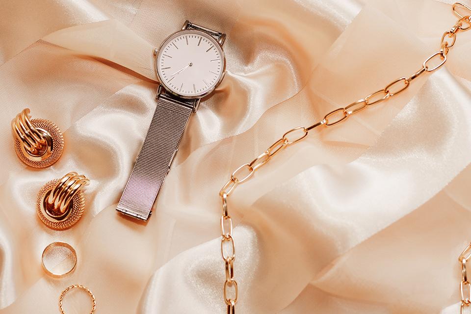 A closeup image of jewellery and a watch on a silk background.
