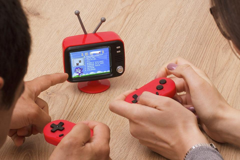 Two people playing on a mini retro game console in red and black.