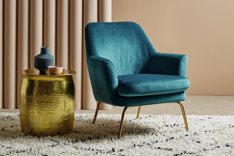 Blue velvet armchair sat on patterned rug next to gold side table.