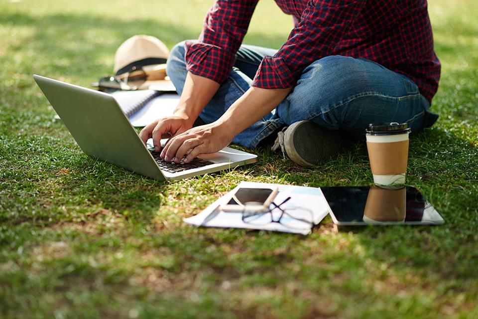 Cropped image of student sitting on the ground and working on laptop.
