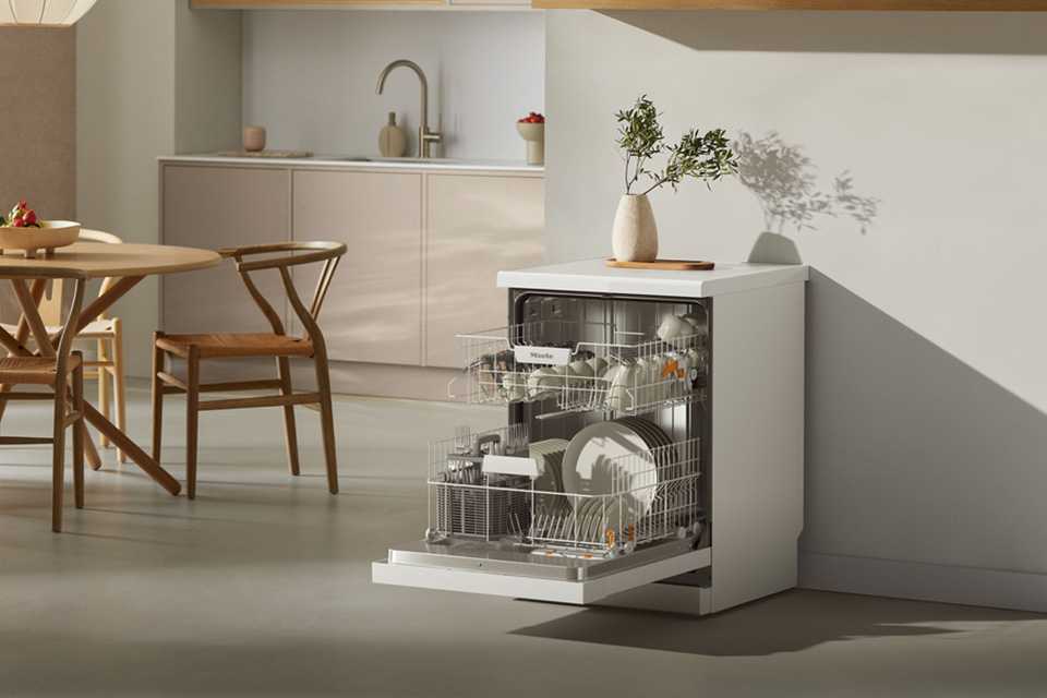An opened Miele dishwasher loaded with plates, mugs and glasses.