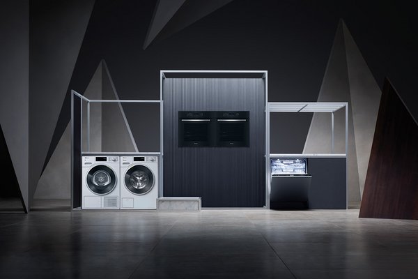 Miele's grey-toned washing machine, tumble dryer, two ovens and a dishwasher on a stage-like setup.