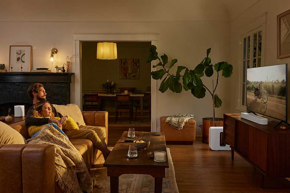 A Sonos soundbar placed under the television with a family watching it.