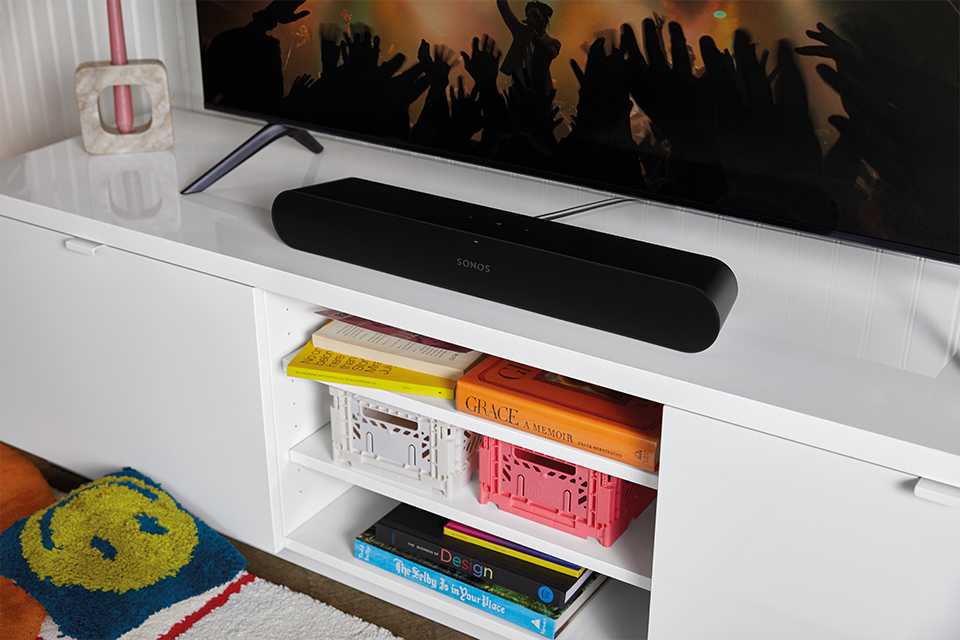 A black Sonos Ray soundbar placed on a white table under a television.