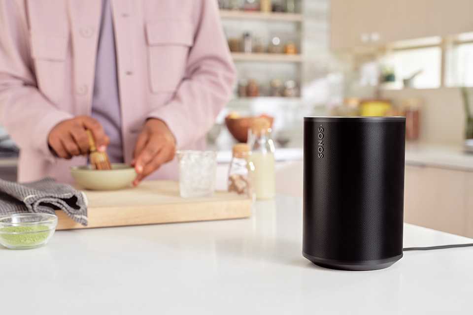 A black Sonos Era 100 bluetooth speaker placed on a kitchentable.