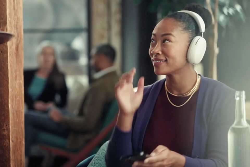 A woman listening to music on Sonos Ace headphone while being served a drink.