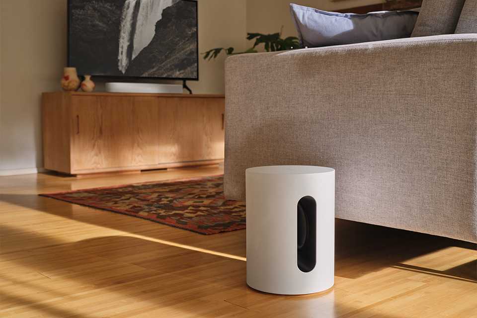 A Sonos Sub Mini subwoofer placed on a wooden floor.