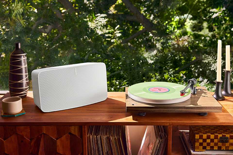 A white Sonos vinyl player placed under the Sun on a wooden table.