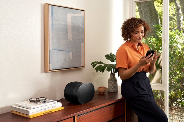 A woman browsing on her phone with Sonos sound system next to her on a table.
