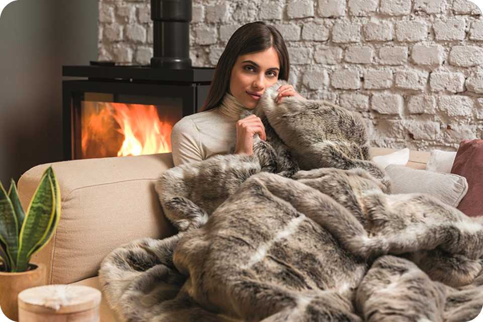 A woman on a sofa underneath the Dreamland Luxury Faux Fur Husky Heated Throw