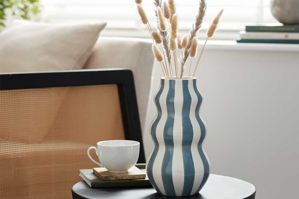 A Habitat blue striped hand-painted vase on a coffee table in a living room.