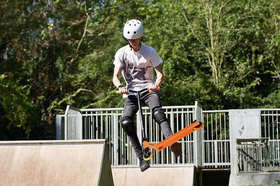 A boy doing stunts on a Zinc Vortex Kids stunt scooter in orange colour.