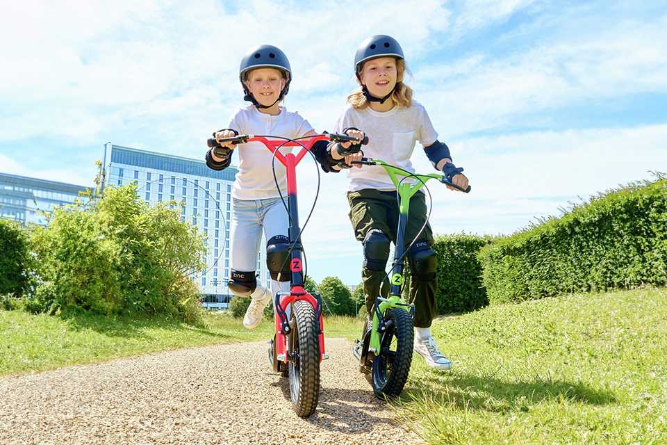 Two girls riding their Zinc Radikal 12 inch Big Wheel BMX scooter outdoors.