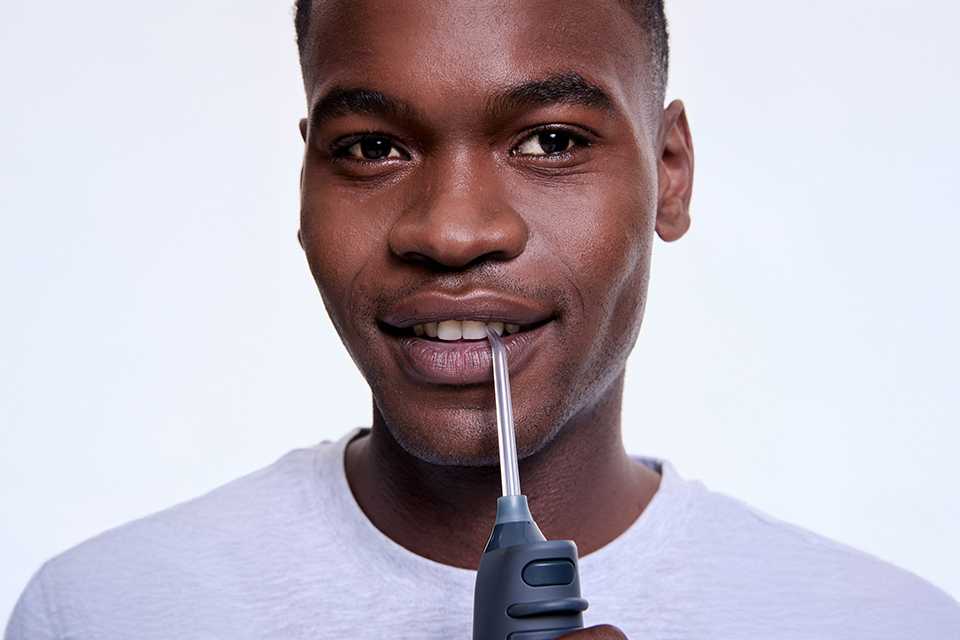 A man flossing his teeth using a graphite black Ordo Hydro Sonic+ water flosser.