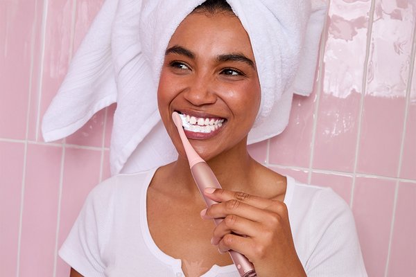Woman in pink tiled bathroom using pink Ordo toothbrush.