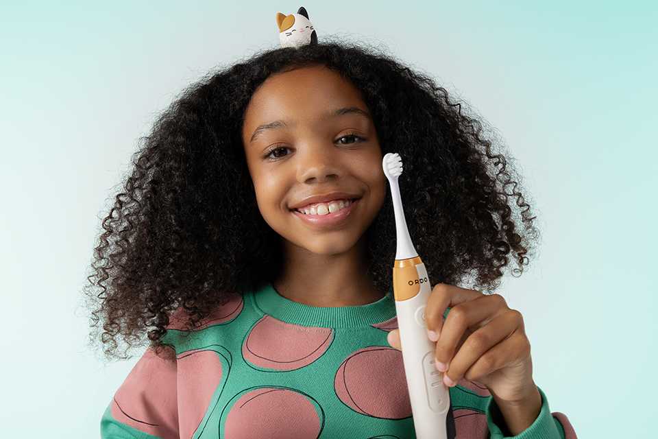 A little girl smiling and holding Ordo Squish Recharge toothbrush.
