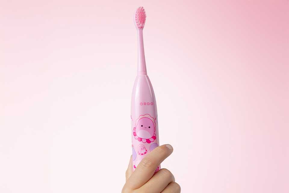 A hand holding the pink Ordo Squishmallow toothbrush up.