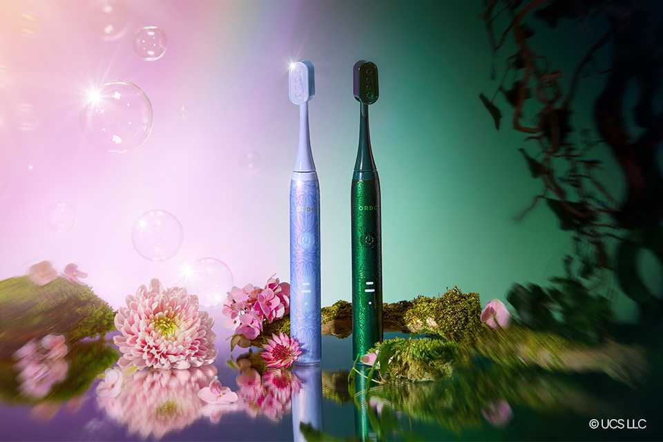 A bluish pink and greenish black toothbrushes against the Wicked pink and green gradient background.