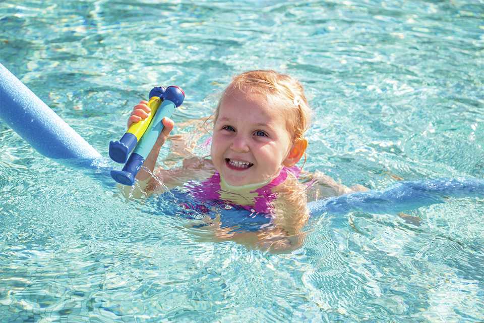 A little girl playing with Zoggs dive sticks in the swimming pool on a summer holiday.