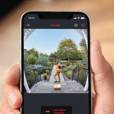 A hand holding a mobile showing the video of a delivery guy in front of the door through Ring battery video doorbell.
