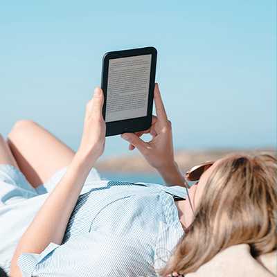 A woman reading from a kindle on a sunlounger on the beach.