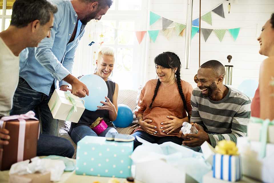 A group of friends at a baby shower, giving gifts and laughing.