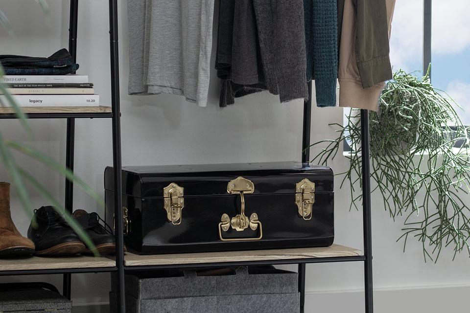 Storage trunk with brass clamps sitting on shelving unit.