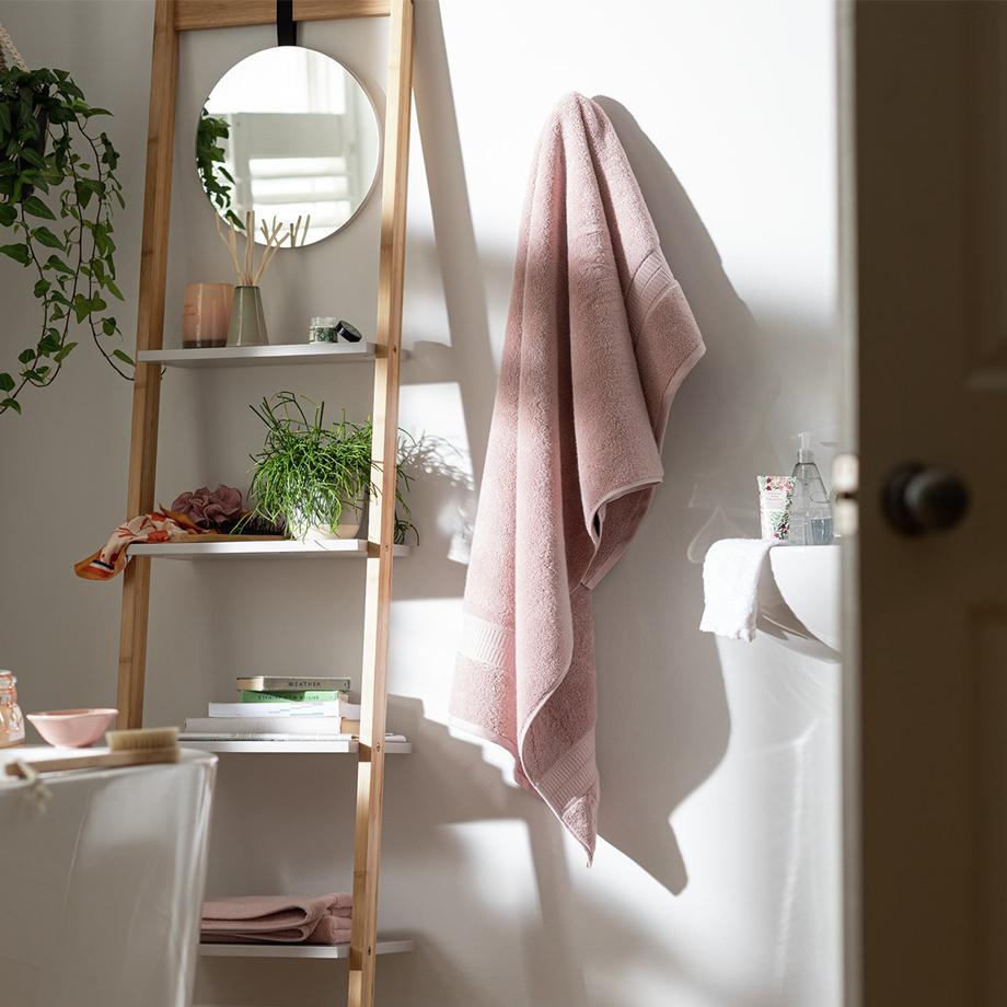 Pink towel hung on a bathroom wall next to a storage shelf.