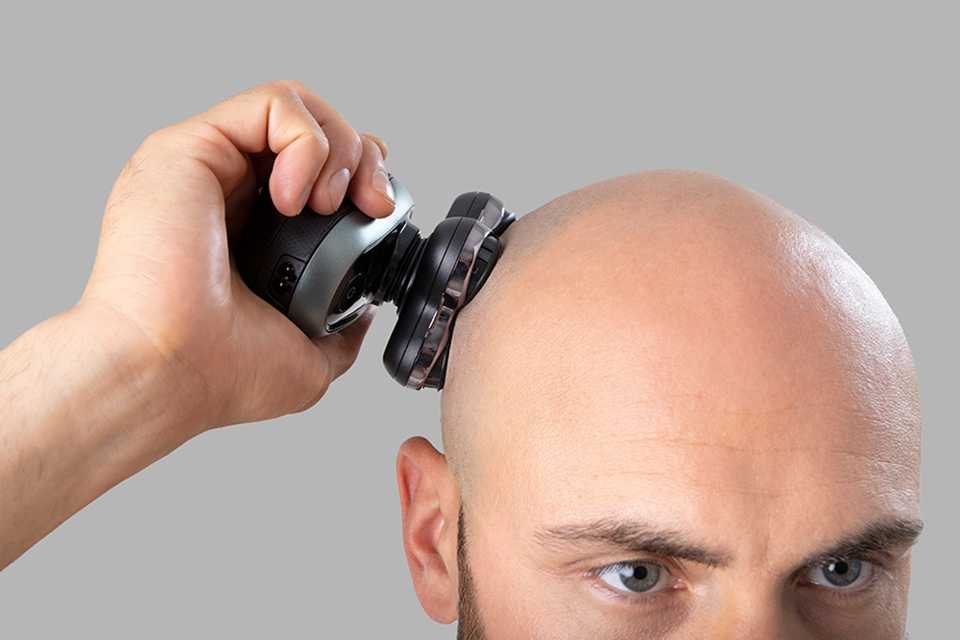A man using Remington head shaver against his bald head.