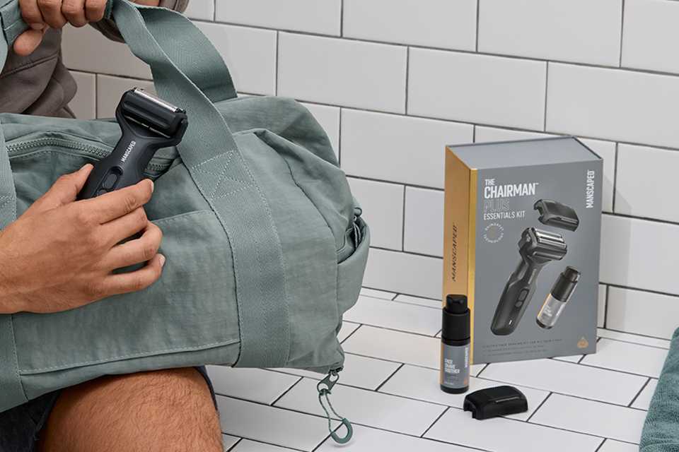 A man holding a duffel bag in one hand and Manscaped Chairman Plus Essentials kit scattered across the bench.