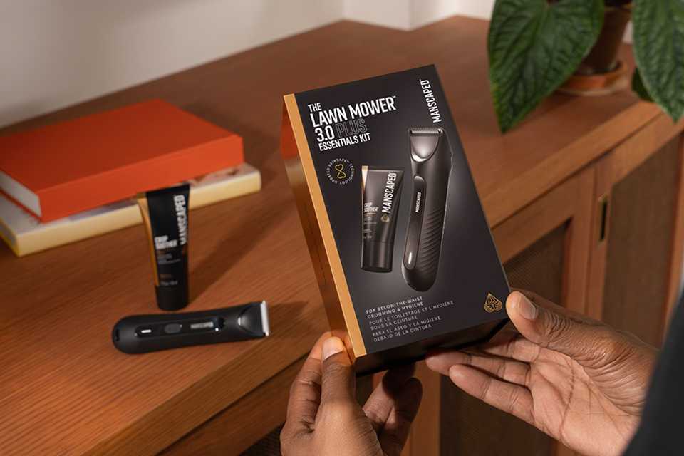 Shot of a person holding Manscaped The Lawn Mover 3.0 Plus box with the product resting on a table.