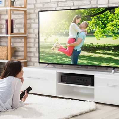 A woman is watching a movie on the TV while lying on a carpet in a living room setup.